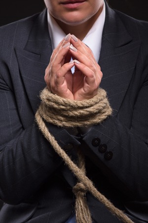 Woman's hands are tied up with strong rope in unbelievable situation. Businesswoman praying to escape as soon as possible.の写真素材