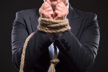 Businesswoman's hands were tied up with strong rope as if she has serious financial problems. Lady in business suit doesn't know what to do.の写真素材