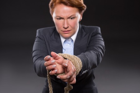 Businesswoman trying to escape from permanent problems in her professional carree. Her hands are tied up with strong rope.の写真素材