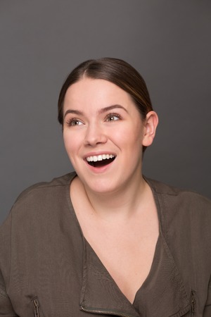 Close-up portrait of happy smiling young lady. Brown-haired lady toothy smiling in photo studio isolated on grey background.の写真素材