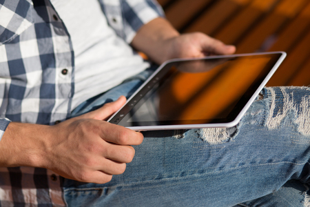 Close-up picture of tablet PC in man's hands. Man in casualsittin on the bench in the park and working with tablet PC, which screen in blank.の写真素材