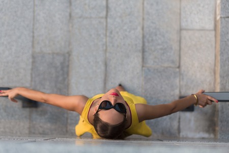 Top view of fashion girl looking at the camera through sunglasses. Brown-haired woman in yellow dress holding hand-rails with both hands.の写真素材