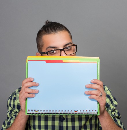 Portrait of fashionable hipster man hiding behind the document and files. Attractive modern man in glasses doesn't want to be caught.の写真素材