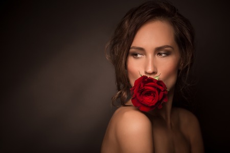 Studio shot. Passionate professional model posing with red rose in her mouth isolated on dark backround.の写真素材