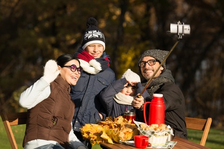 Happy young family making selfies while sitting at the wooden table. Parents and children posing and smiling for the camera.の写真素材