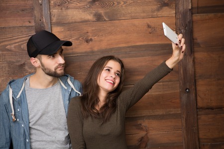 Happy friends making selfies isolated on wooden background. Beautiful brunette holding camera in front of her.の写真素材