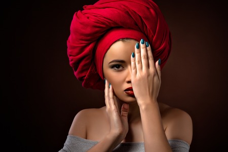 Beautiful latin girl hiding behind her palm isolated on dark. Attractive lady with red lips touching her cheek.の写真素材