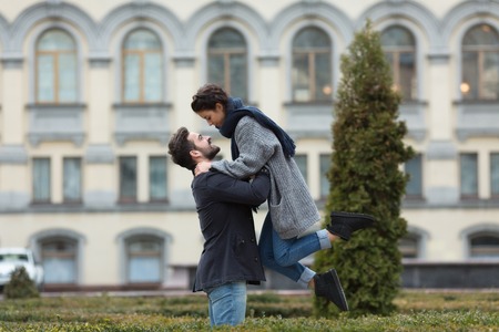 Happy couple enjoying the day in the autumn park. Handsome and strong man lifting his girl-friend from excitement.の写真素材