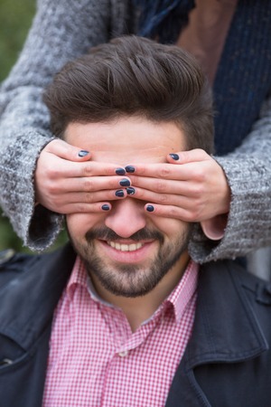 Woman closing the eyes of handsome man while he is smiling. Lady dreaming about surprise for him.の写真素材