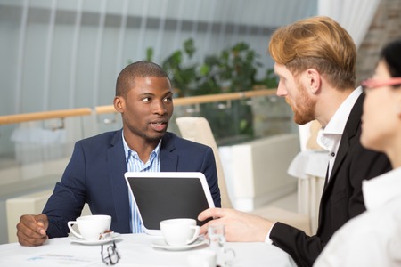 Communication betweent business people during business meeting in restaurant. People sitting at table and looking at tablet PC.の写真素材