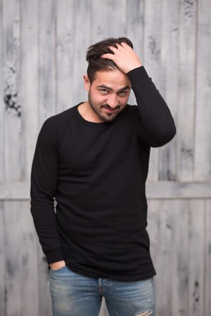 Portrait of brunette model man in black pullover posing in studio. Handsome man combing his hair and keeping one hands in pocket.の写真素材