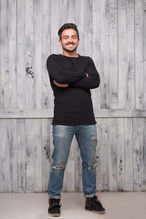 Brunette model man posing in full length with his arms crossed over white background. Man in black sweater and jeans smiling.の写真素材