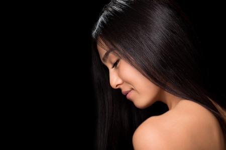 Close-up profile of smiling asian lady with gorgeous black hair in studio. Naked young lady looking down and happy smiling.の写真素材