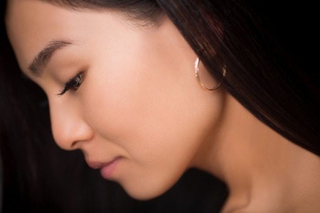 Close-up profile of beautiful professional asian model lady in studio. Young lady with black hair looking down and posing for photographer.の写真素材