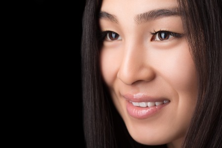Close-up of smiling Asian woman over black background. Happy lady with long black hair looking away and posing for camera. Copyspace in studio.の写真素材