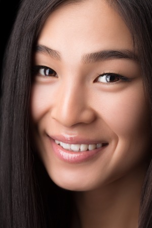 Close-up portrait of smiling Asian woman in studio. Happy toothy laughing lady with long hair looking at camera over black.の写真素材