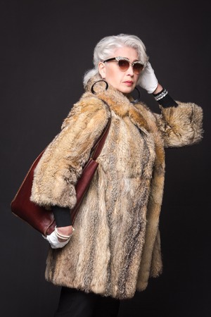 Senior rich woman posing for fashion or vogue magazine isolated on black background. Beautiful lady in expensive fur coat.の写真素材