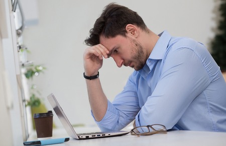Handsome man thinking about business projects and strategies over laptop computer in restaurant or...