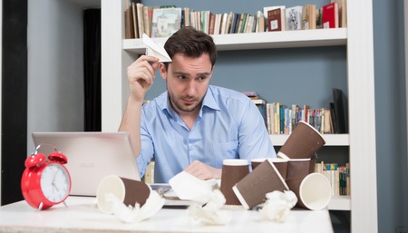 Tired male freelancer looking at carton cups of tea or coffee in library. Hnadsome man looking...