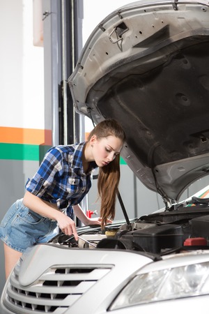 Beautiful worker woman repairing engine or motor at service station. Long-haired lady in sexy clothes working at repair shop.の写真素材