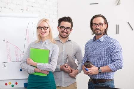 Portrait of happy business people looking at camera while standing in office near while board....