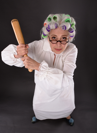 Top view of crazy furious grandmother holding criket bat and looking at camera. Beautiful lady with rollers on in studio.の写真素材