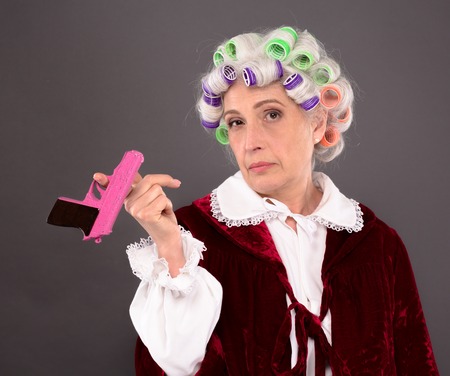 Grandmother with rollers on posing with pink plastic gun over grey background. Serious lady looking...