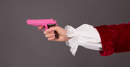 Close-up of pink plastic gun over grey background. Woman's hand holding child's toy in studio.の写真素材