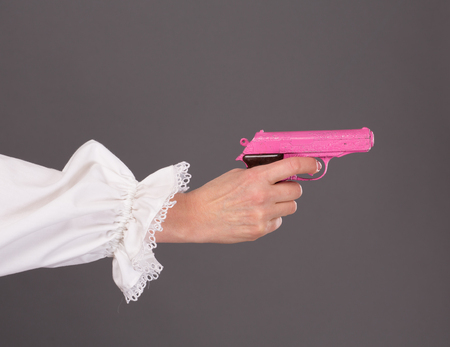 Close-up picture of child's pink plastic gun in studio. Lady's hand holding toy over grey background.の写真素材