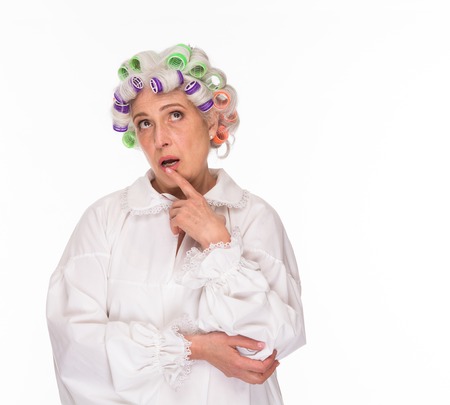 Thoughtful senior lady posing over white background and looking upwards in studio. Modern grandmother with rollers on posing for photographer for fashion magazine.の写真素材