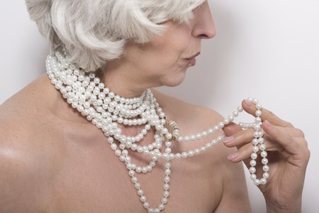 Closeup portrait of mature naked woman demonstrating her expensive beads in studio over white background. Naked concept.の写真素材