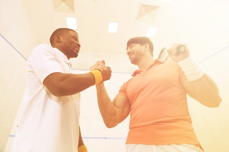 Competition between two best friends playing squash. Low view of handsome men standing face to face and shaking hands.の写真素材