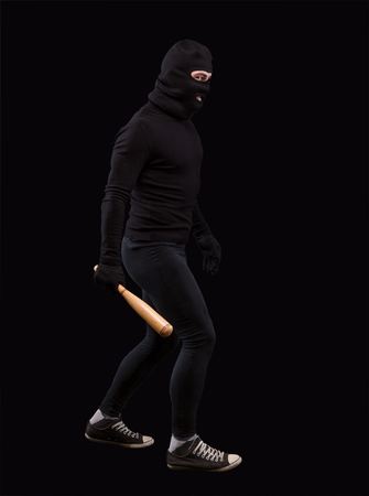 Man in black with black mask on. Burglar going to steak something or someone. Man holding bat over black background. Isolated on black.の写真素材