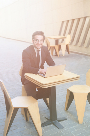 Toned picture of handsome businessman in glasses sitting at table in restaurant or cafe. Freelance man using laptop computer. Man looking at camera.の写真素材