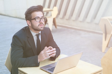 Toned image of serious and confident businessman using laptop computer for work while sitting in restaurant or cafe. Freelance man looking upwards.の写真素材