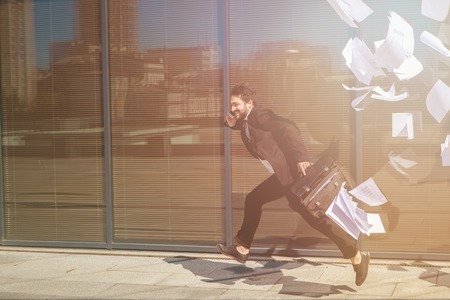Toned picture of running businessman along street with briefcase and speaking over mobile or smart phone. Freelance man in hurry.の写真素材