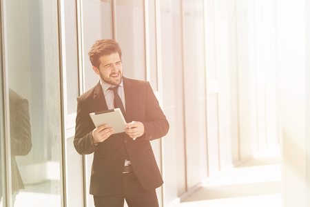 Toned image of businessman or freelancer walking along street with tablet PC in his hands. Happy man in business suit looking away in distance.の写真素材