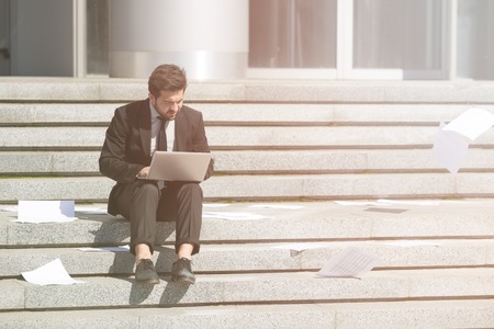 Toned picture of handsome businessman sitting on stairs incity centre and using laptop computer for business purposes.の写真素材