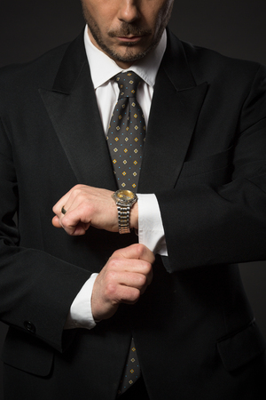 Closeup of businessman in black suit correcting sleeve in studio. Man preparing for work or business meeting.の写真素材