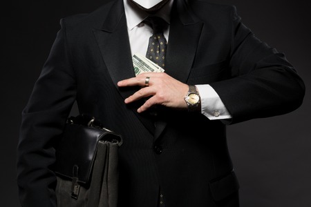 Businessman hiding money in jacket pocket. Corruption and fraud concepts. Man in business suit posing with black briefcase.の写真素材