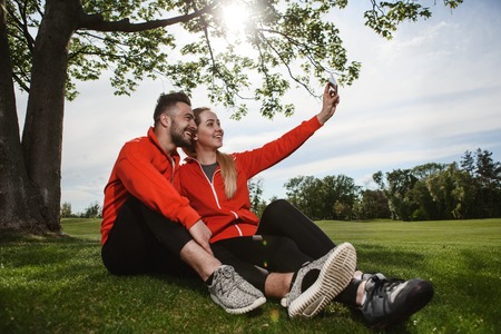 Sport man and woman making selfies in green park or forest while resting and relaxing after hard-working day. Fitness, sportrs and lifestyle concepts.の写真素材