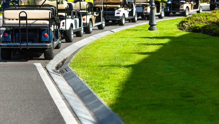 Golf carts not far from golf course. White golf carts at green golf course. Golf landscape in spring day.の写真素材
