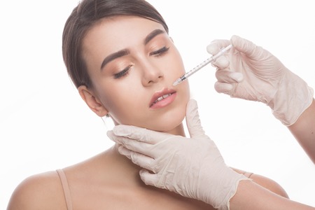 Closeup of beautiful woman getting injections in her lips. Full lips. Beautiful face and syringe. Plastic surgery and cosmetic injection concepts.の写真素材