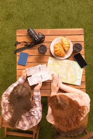 Top back vie of pretty ladies sitting at table in park and looking at mapor guide for finding interesting places for sightseeing. Tourism concept.の写真素材