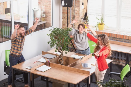 Happy business people showing teamwork in office. Cheerful people standing with their arms raised while having round table.の写真素材