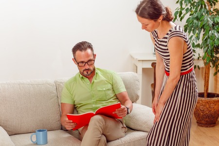 Portrait of handsome man looking at documents while his wife standing near him. Businessman preparing for meeting from home.の写真素材