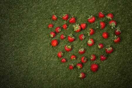 Fresh strawberries background represented in form of heart. Background of freshly harvested strawberries represented on green grass.の写真素材