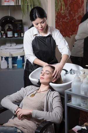 Side view of beautiful hairdresser washing hair to her client lady in hairdressing saloon. Client sitting with her eyes closed.の写真素材