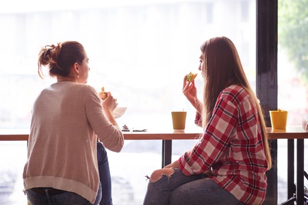 Toned picture of back view of beautiful ladies sitting in cafe or restaurant near window. Girls...