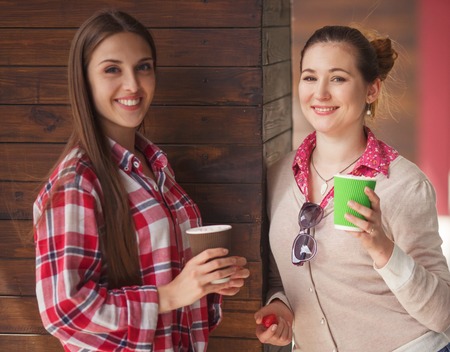 Toned picture of happy smiling girls communicating or talking near restaurant or cafe. Beautiful ladies drinking cups of coffee outdoors.の写真素材